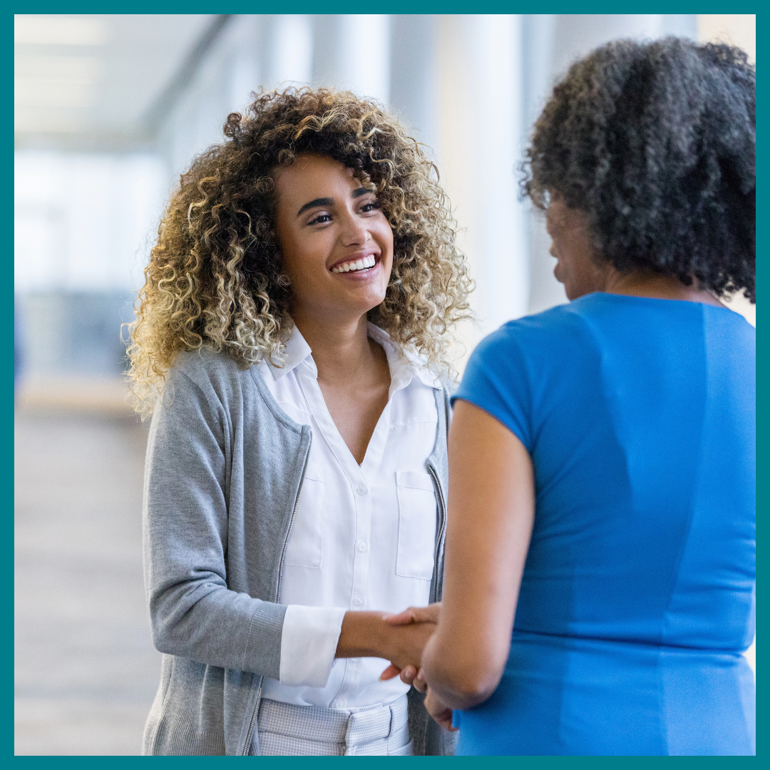 Two professional Black women smile while shaking hands